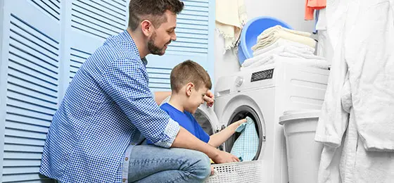 The picture shows a father and his son filling a washing machine.